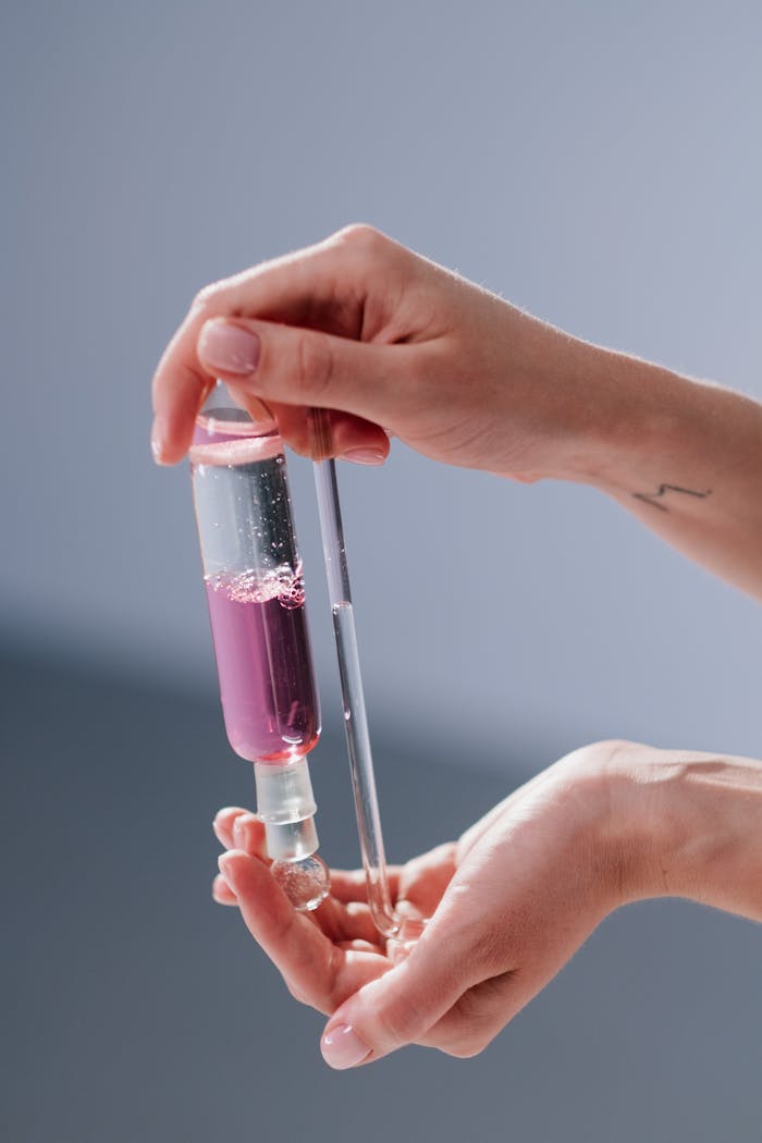 Close-up of hands with tattoos holding a test tube containing pink liquid.